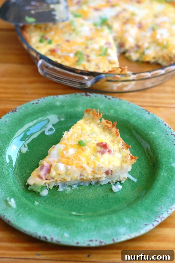 Delicious Hash Brown Crust Breakfast Casserole with ham, cheese, and eggs on a plate. A delicious slice of Hash Brown Crust Breakfast Casserole, showcasing the crispy golden hash brown crust, melted cheese, fluffy eggs, and savory ham, served on a white plate ready to be enjoyed.
