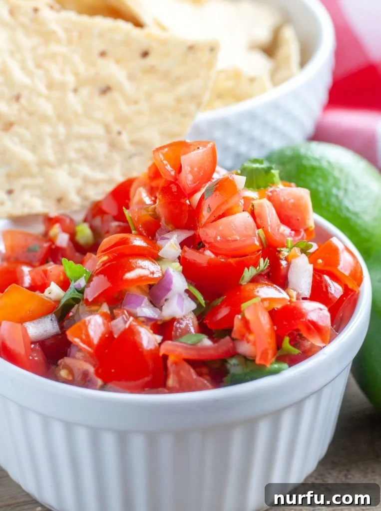 Fresh and Zesty Salsa 2 Vibrant Pico de Gallo in a white bowl, garnished with a tortilla chip and lime wedges, showcasing its freshness.