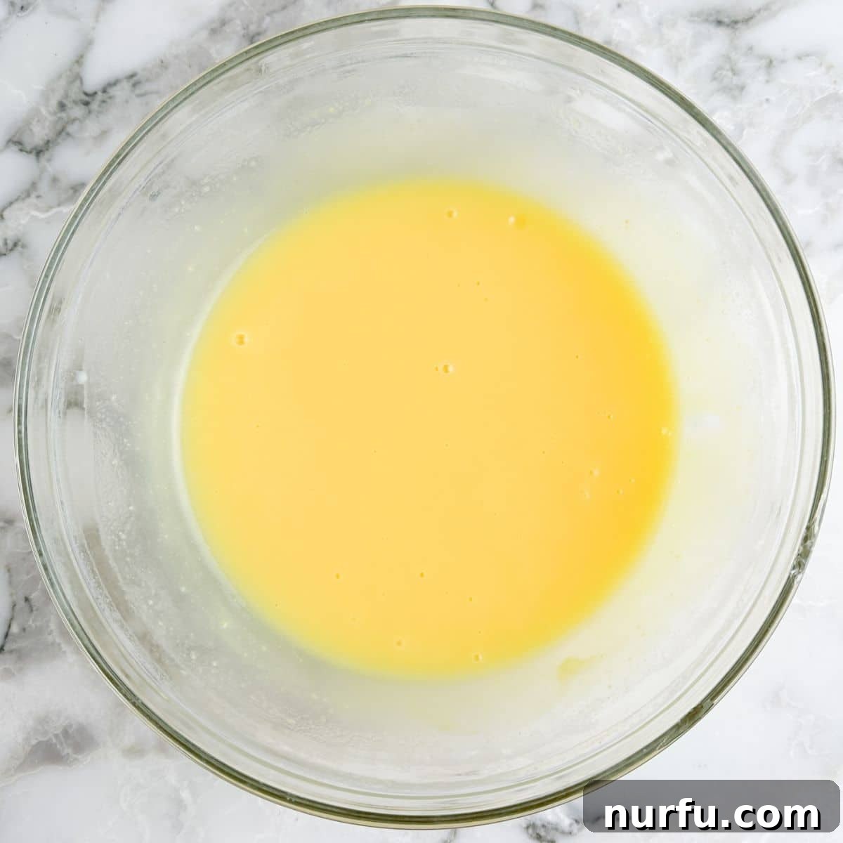 A bowl containing whisked instant vanilla pudding and milk, beginning to thicken.