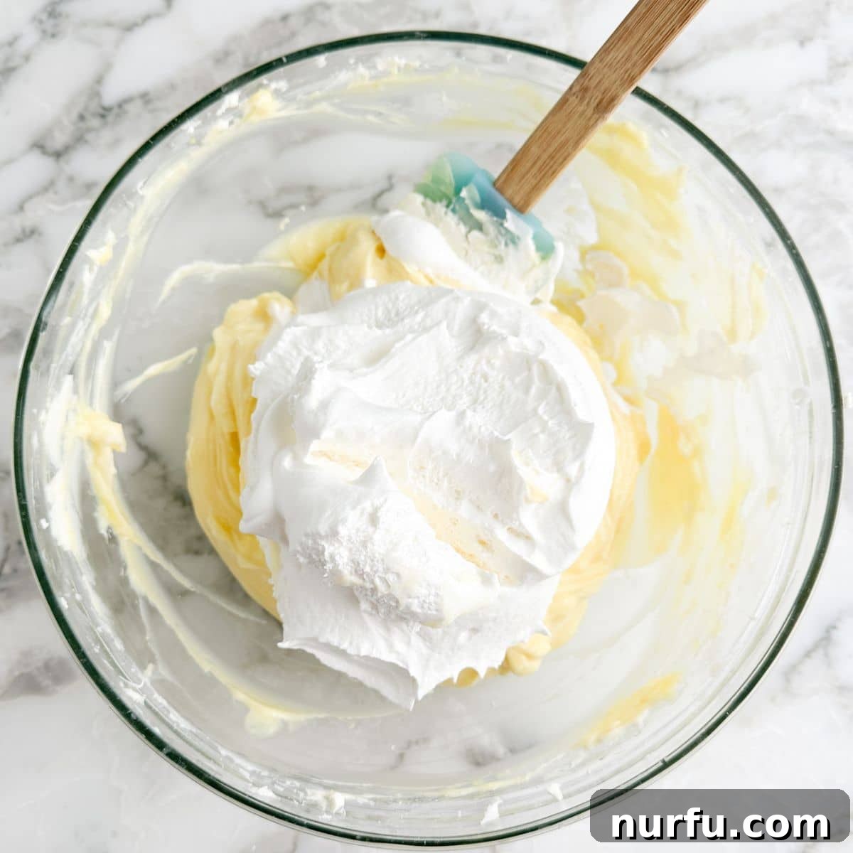 A bowl containing the combined vanilla pudding and cream cheese mixture, with thawed whipped topping being folded in.