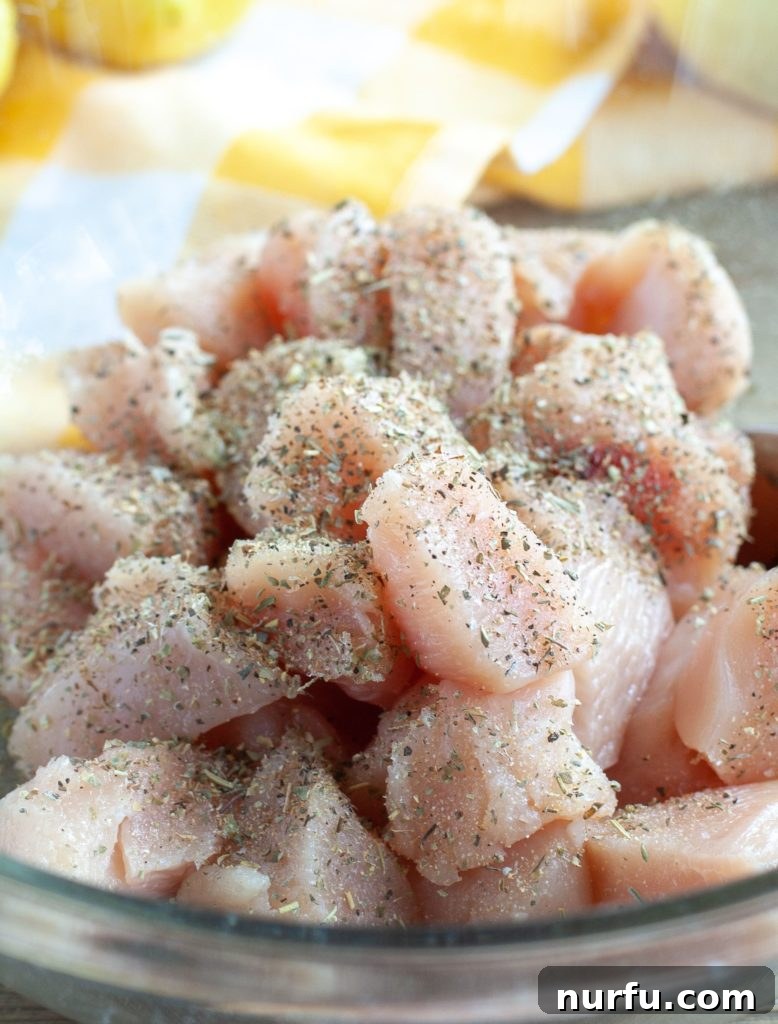 Seasoned Chicken Diced chicken breast seasoned with herbs, spices, lemon, and olive oil in a clear glass bowl, ready for cooking.