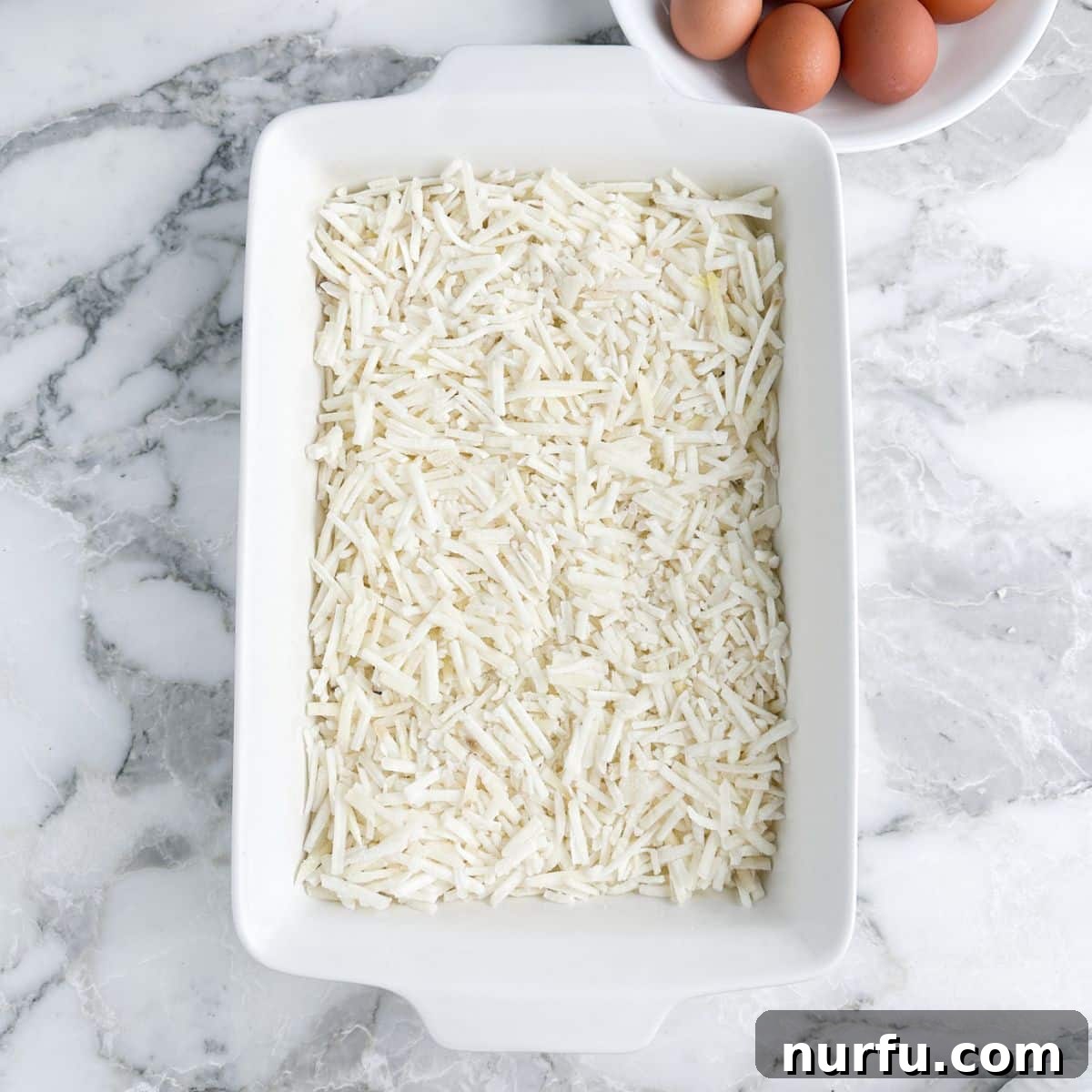 Hearty Farmhouse Casserole 3 A 9x13 casserole dish evenly filled with a layer of frozen shredded hash browns, ready for additional ingredients.