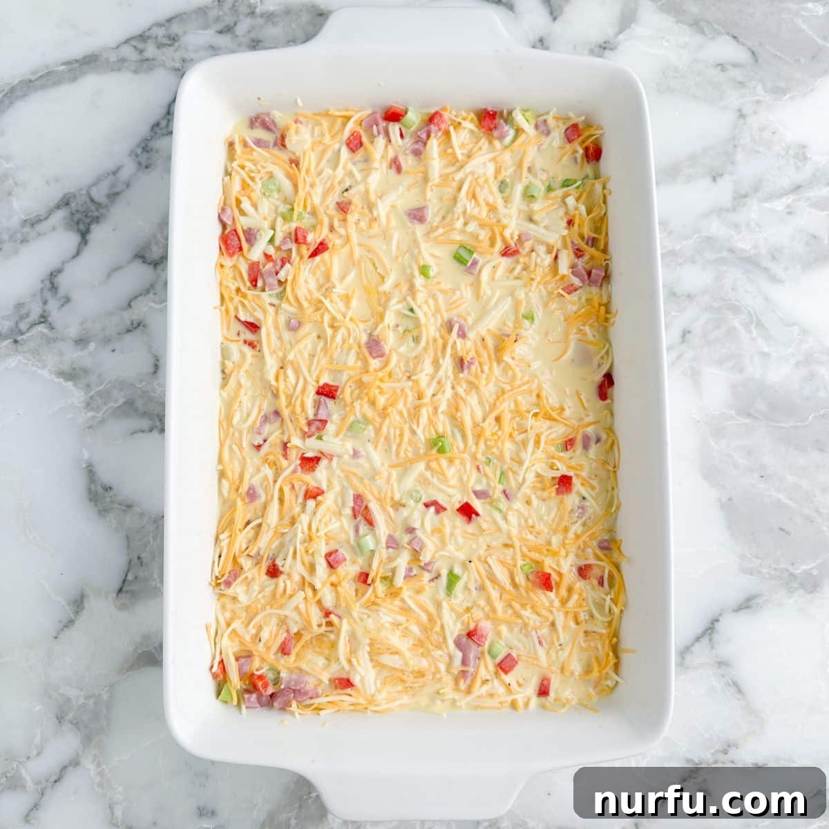 Hearty Farmhouse Casserole 6 The breakfast casserole in a baking dish, with the egg and milk mixture being poured evenly over the layers of hash browns, ham, vegetables, and cheese.