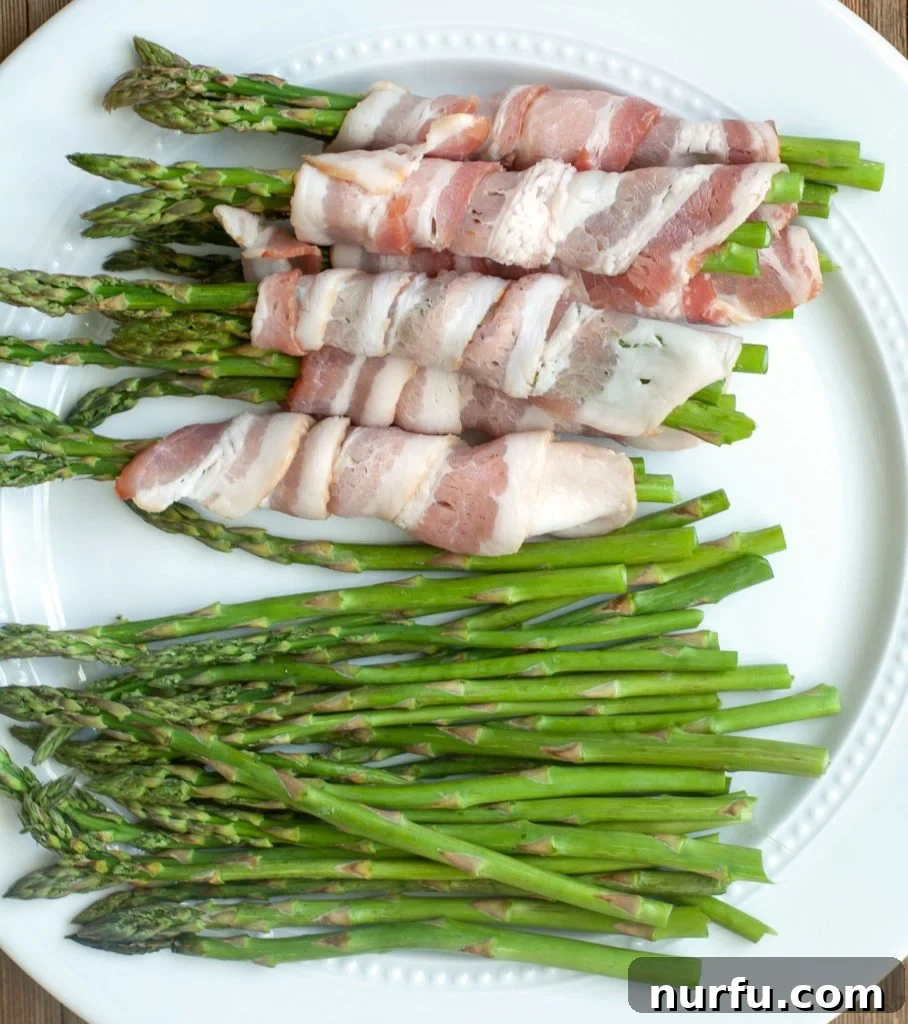 Air Fryer Bacon Wrapped Asparagus Fresh asparagus spears being wrapped in strips of bacon on a cutting board, ready for the air fryer