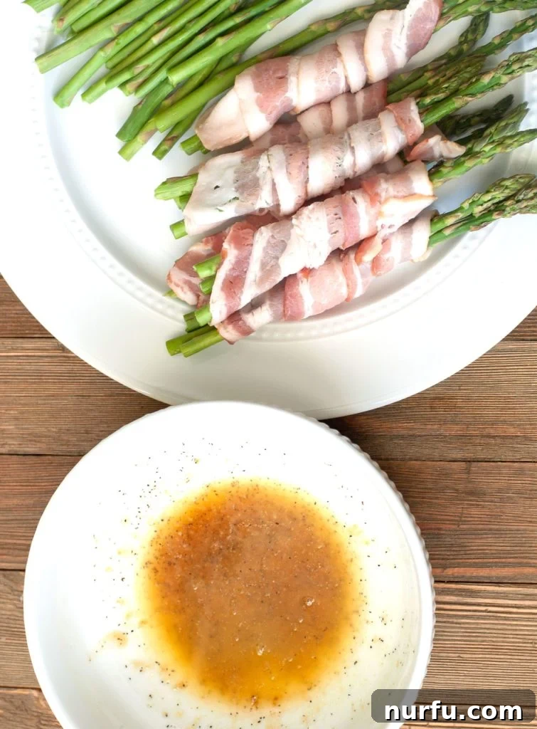 Air Fryer Bacon Wrapped Asparagus Bowl of melted butter and brown sugar glaze next to bacon-wrapped asparagus bundles, ready for brushing