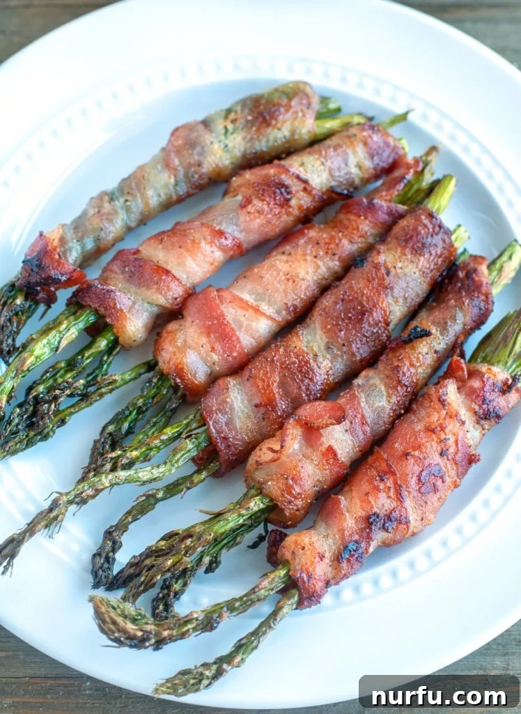 Air Fryer Bacon Wrapped Asparagus Top-down view of cooked Bacon Wrapped Asparagus on a white plate, garnished and ready to serve