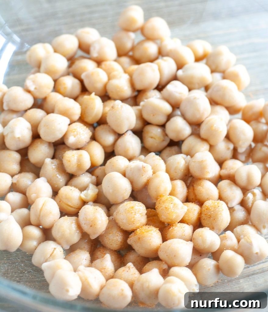 Air Fryer Roasted Chickpeas Chickpeas in a glass bowl, coated with olive oil and seasoned salt.