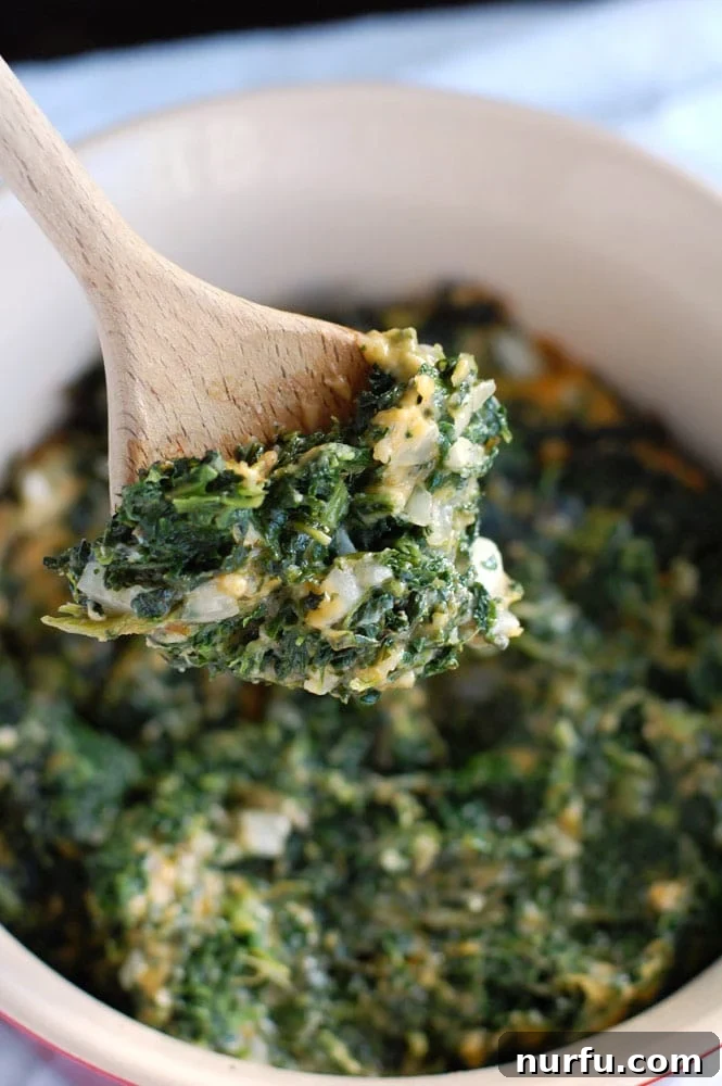 Deviled Spinach A wooden spoon holds a serving of creamy, cheesy spinach casserole, highlighting its rich texture and appetizing appeal.