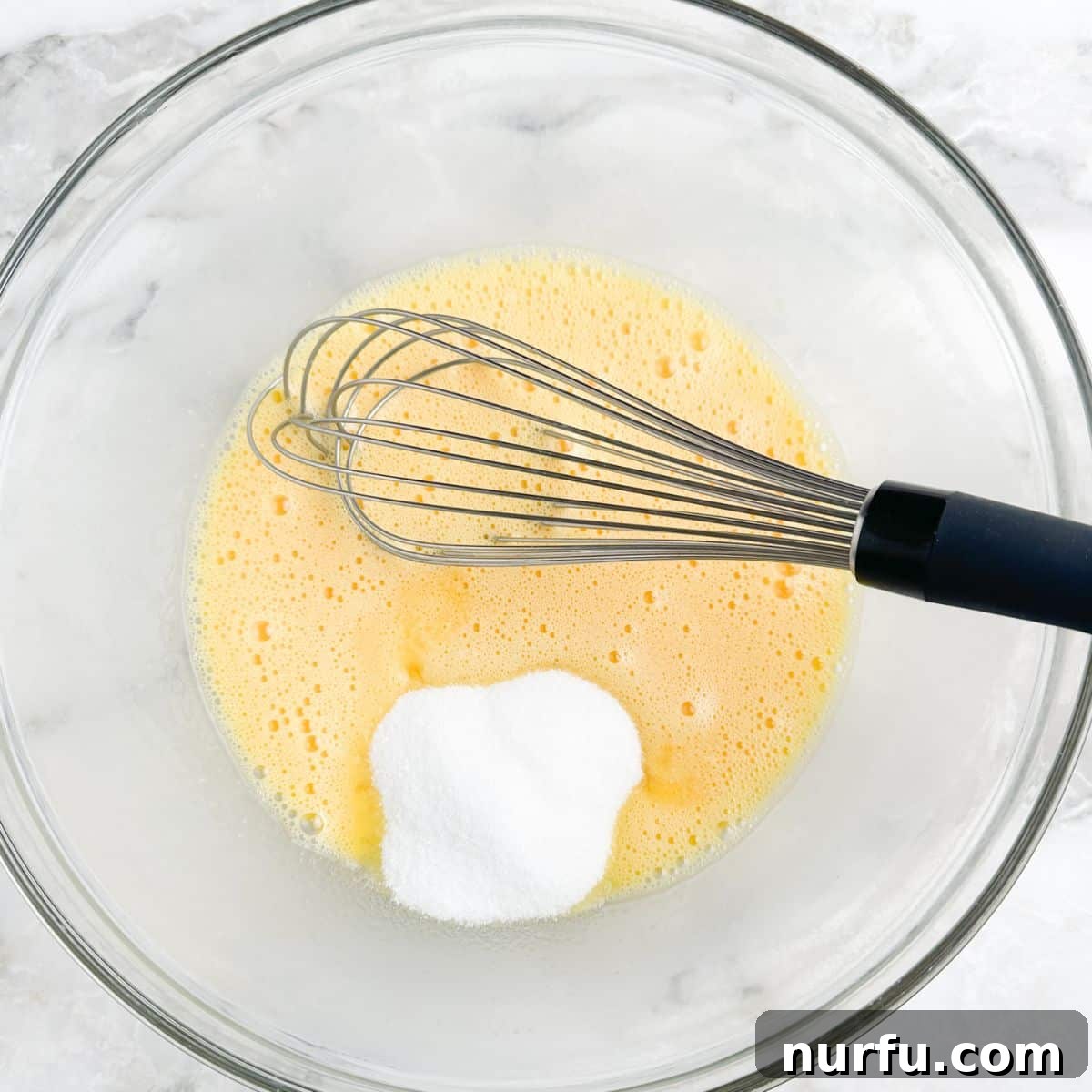 Effortless Velvety Egg Custard 4 A glass bowl containing beaten eggs and sugar, with a whisk resting inside.