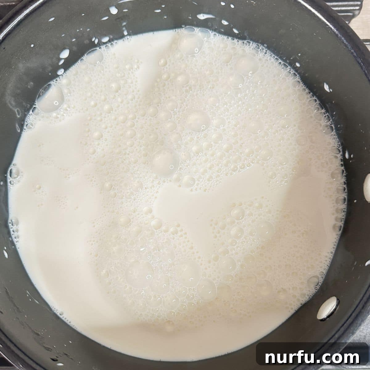 Effortless Velvety Egg Custard 5 A stainless steel saucepan on a stovetop, with milk gently warming inside.