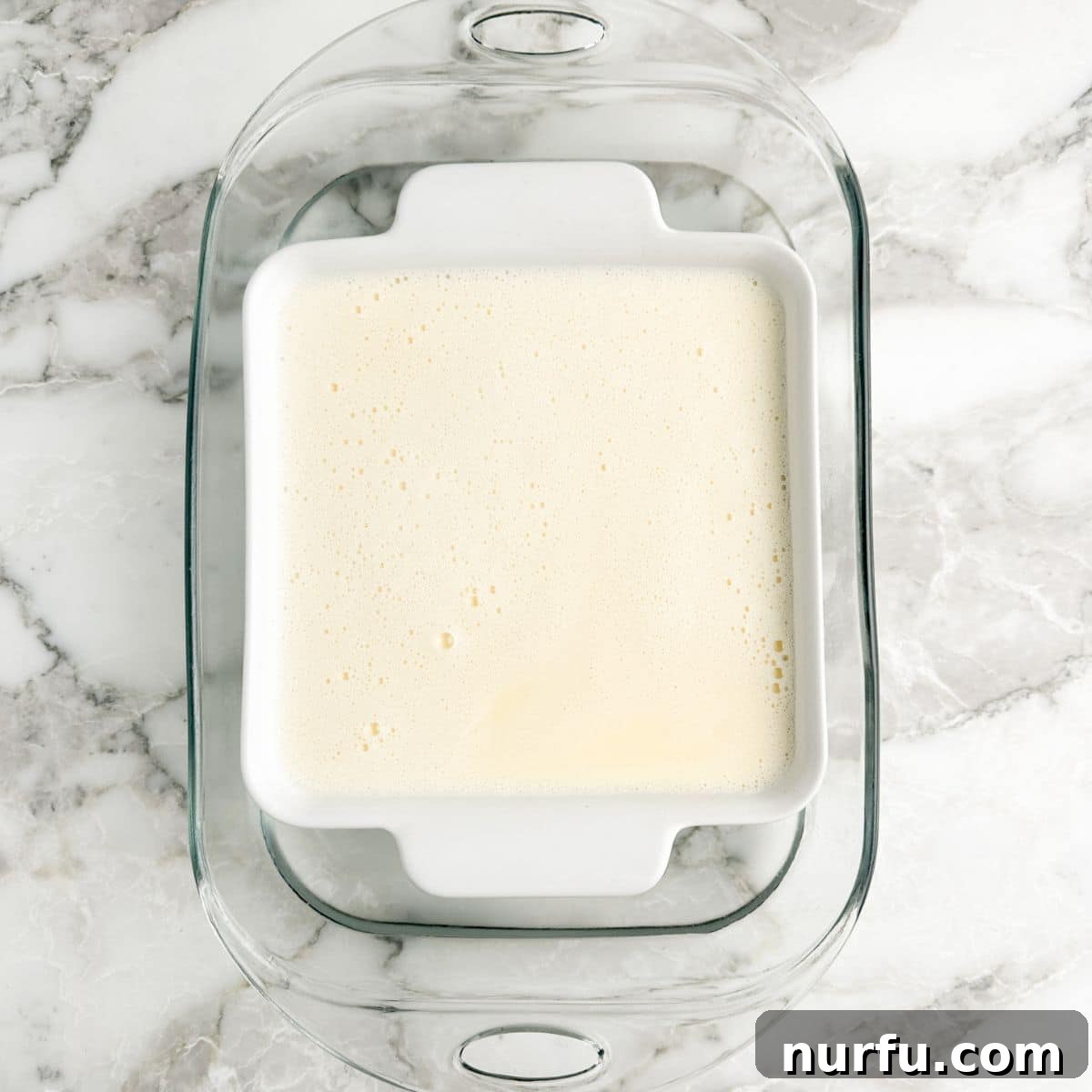 Effortless Velvety Egg Custard 6 A baking dish filled with egg custard, placed within a larger baking dish partially filled with water, ready for baking.