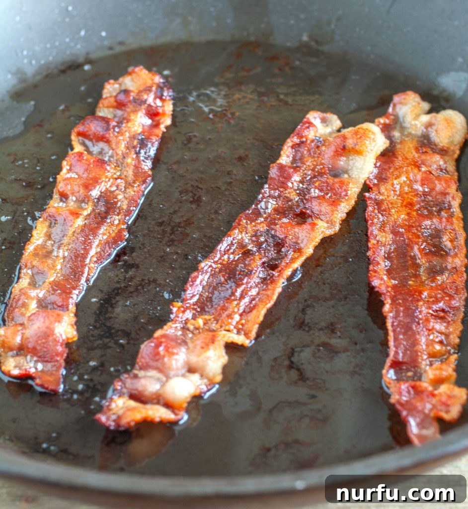 Fried Corn Three pieces of bacon sizzling in a cast-iron skillet, ready to render its flavorful grease for the fried corn