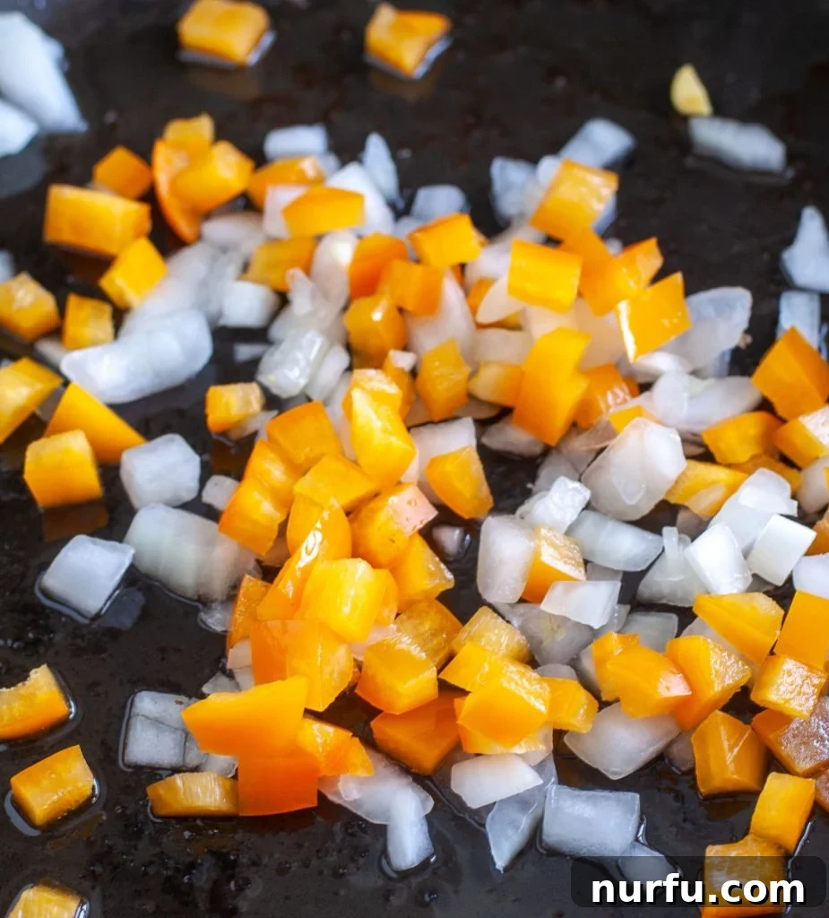 Fried Corn Finely diced onion and vibrant orange bell pepper gently cooking in a skillet with bacon grease, preparing the flavor base for the fried corn