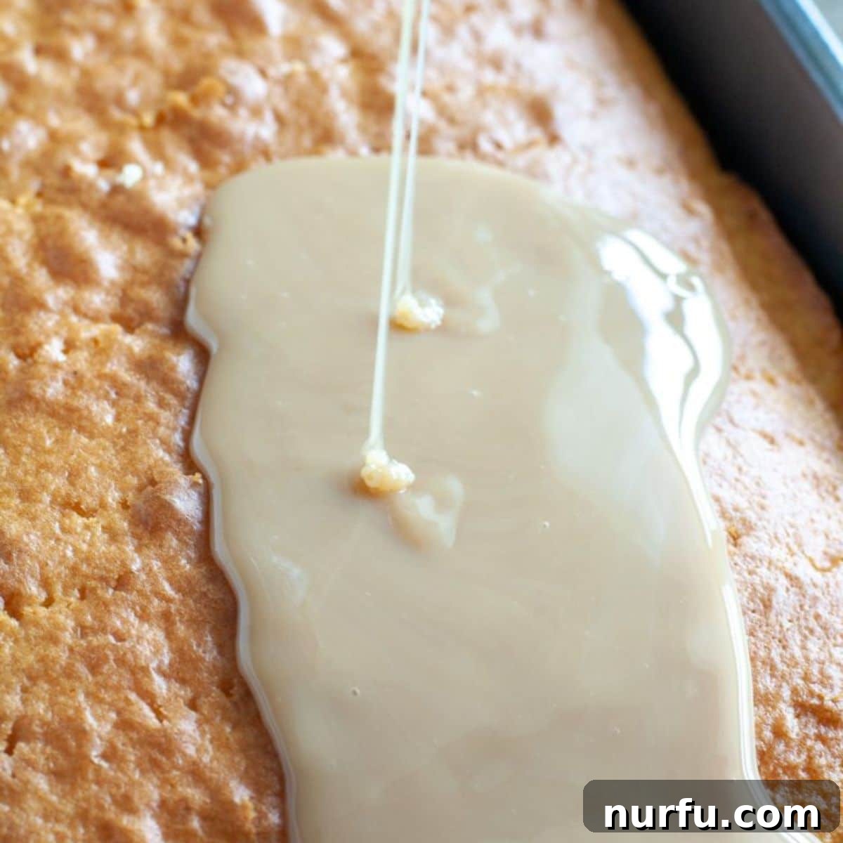 Golden Crunch Butterfinger Poke Cake 4 Sweetened condensed milk and caramel sauce being poured over a poke-filled yellow cake, ready to soak into every crevice.