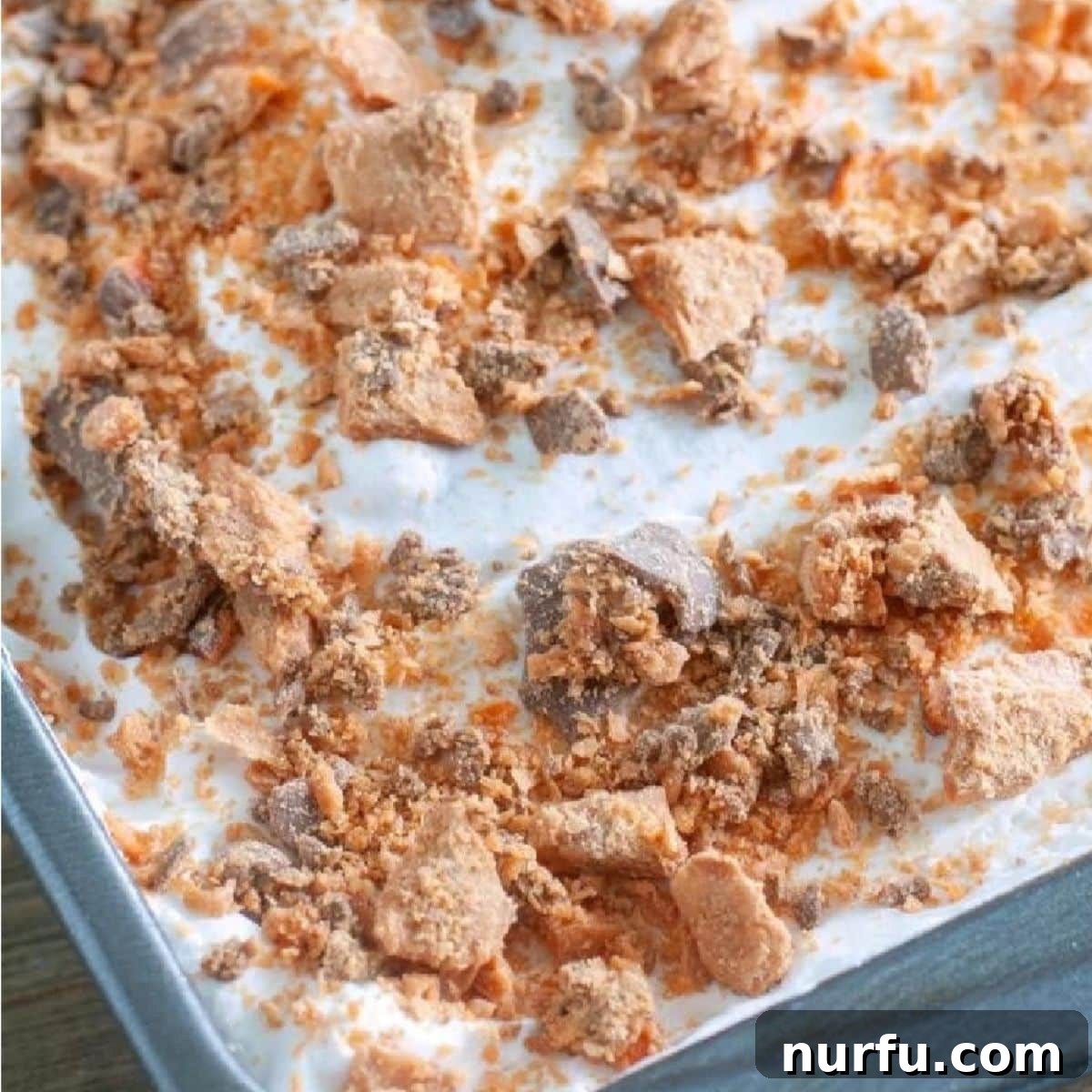 Golden Crunch Butterfinger Poke Cake 5 A finished Butterfinger poke cake, topped with fluffy whipped cream and a generous layer of crushed Butterfinger candy, ready to be served.