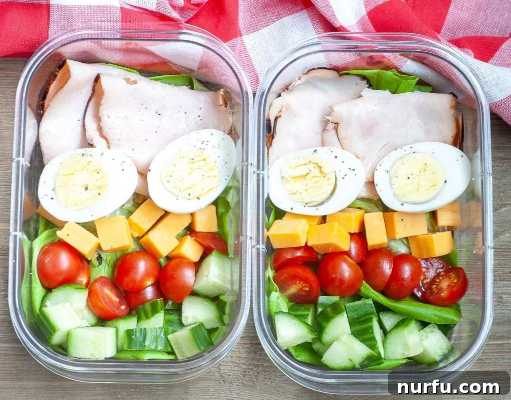 Keto Meal Kit Two meal prep containers with sliced turkey, hard-boiled eggs, cheese cubes, cherry tomatoes, and cucumber slices, ready for a keto snack.