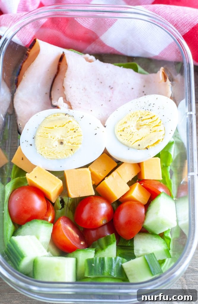 Keto Snack Box A single meal prep container loaded with turkey slices, a hard-boiled egg, cheese cubes, cherry tomatoes, and cucumber slices.