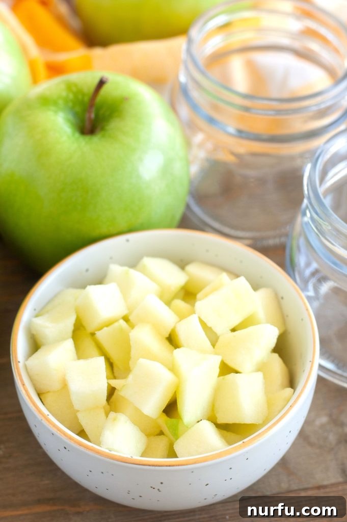 Prepared Apples for Filling A bowl of freshly diced apples, with empty glass jars and a whole apple in the background.