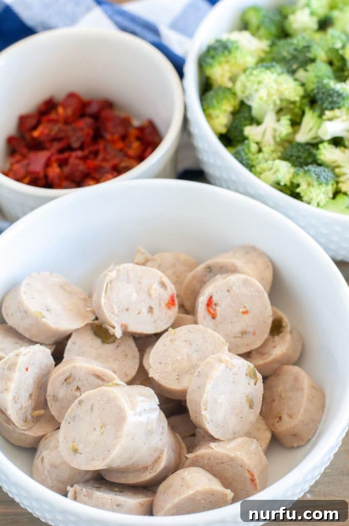 Orecchiette with broccoli and chicken sausage Individual bowls holding prepped chicken sausage slices, sun-dried tomatoes, and fresh broccoli florets, showcasing ingredients ready for cooking.