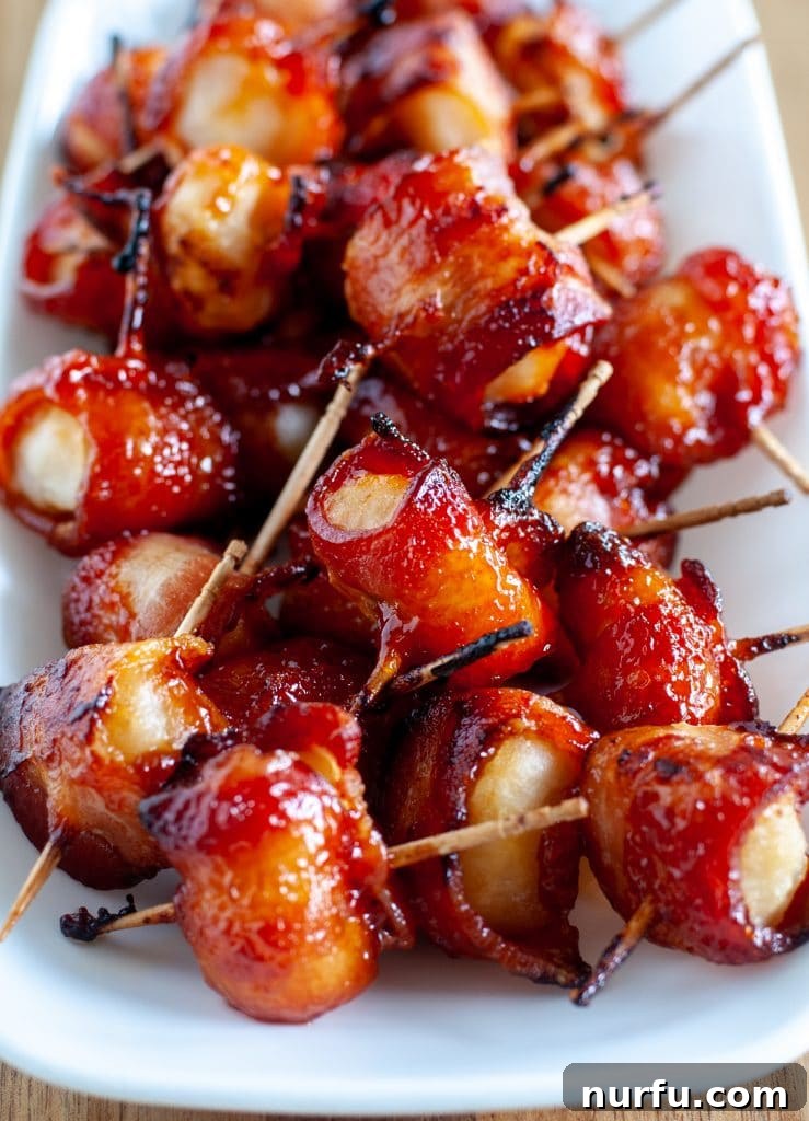 Crispy Bacon Wrapped Water Chestnuts 2 Crispy bacon wrapped water chestnuts on a white plate, glistening with a sweet glaze.