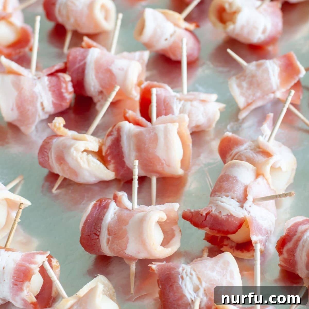 Crispy Bacon Wrapped Water Chestnuts 4 Several bacon wrapped water chestnuts, secured with toothpicks, neatly arranged on a baking sheet lined with foil.