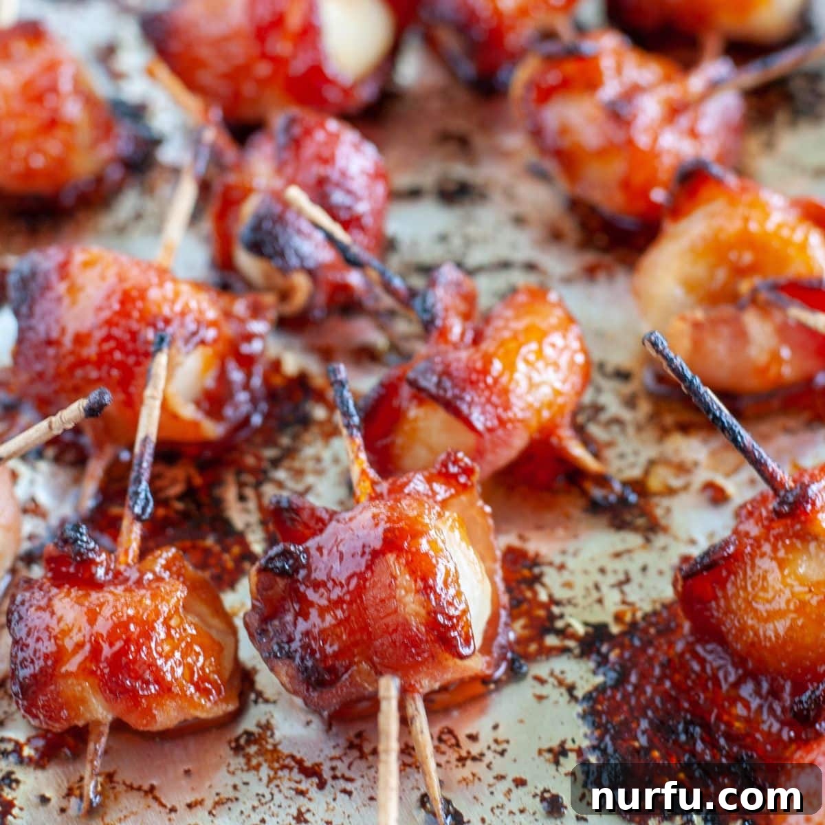 Crispy Bacon Wrapped Water Chestnuts 6 Freshly baked bacon wrapped water chestnuts, glistening with a caramelized glaze, on a foil-lined baking sheet.