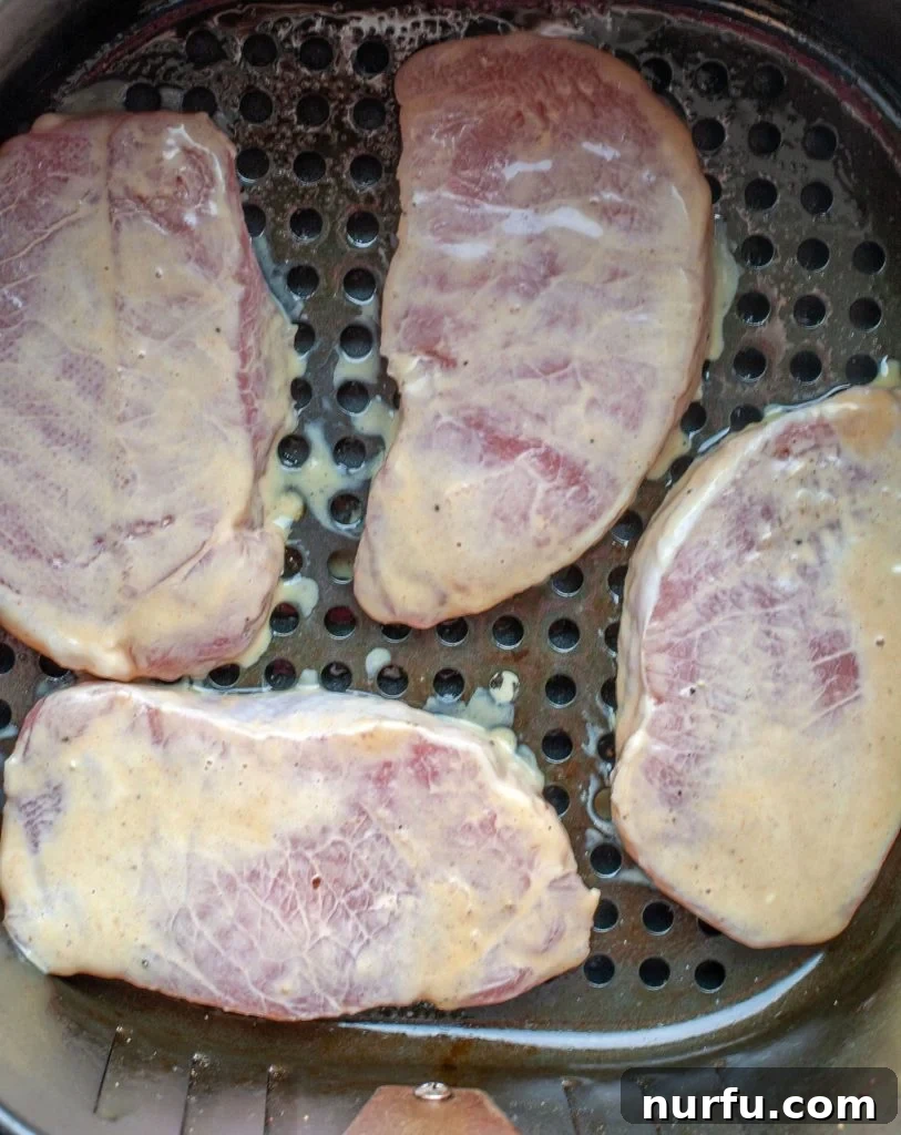 Air Fryer Pork Chops cooking in the basket Four perfectly spaced honey mustard pork chops cooking to a golden crisp in the basket of an air fryer.