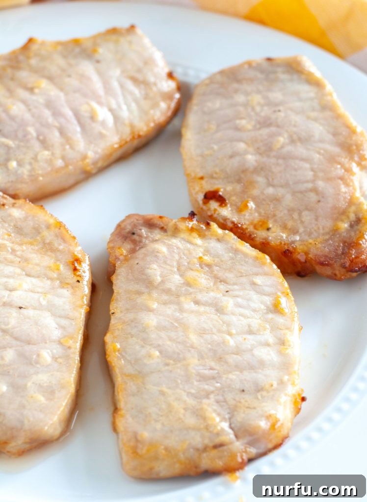 Cooked Air Fryer Pork Chops ready to serve Four perfectly cooked and glazed Air Fryer Honey Mustard Pork Chops neatly arranged on a pristine white serving plate.