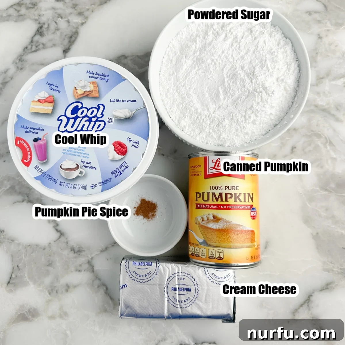 Velvety Pumpkin Spice Dip 3 An organized arrangement of the five essential ingredients for pumpkin dip: a tub of Cool Whip, a bowl of powdered sugar, a small bowl of pumpkin pie spice, a can of pure pumpkin, and a block of softened cream cheese, all laid out on a kitchen counter.