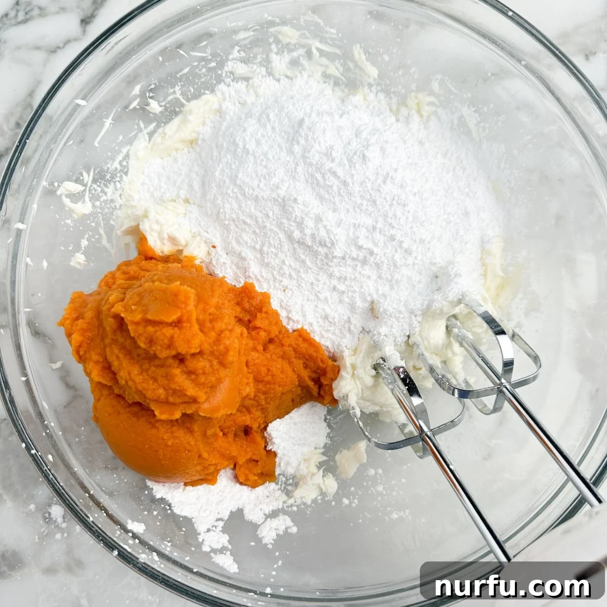 Velvety Pumpkin Spice Dip 5 In a mixing bowl, beaten cream cheese is combined with pure canned pumpkin, powdered sugar, and pumpkin pie spice, forming a rich, orange mixture ready for final blending.