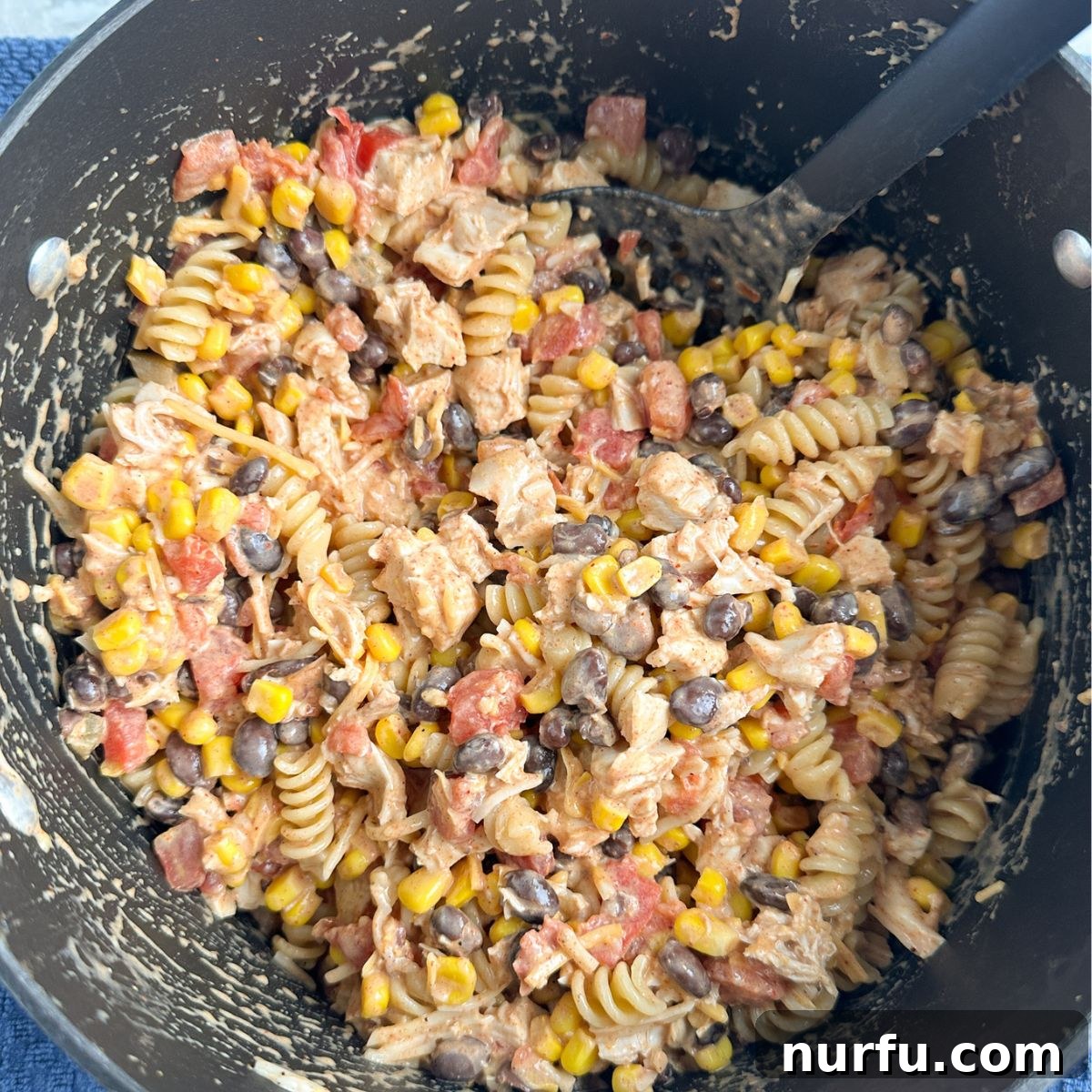 Celebration Chicken Bake 6 Pot with a pasta, chicken, and bean mixture, stirred and combined.