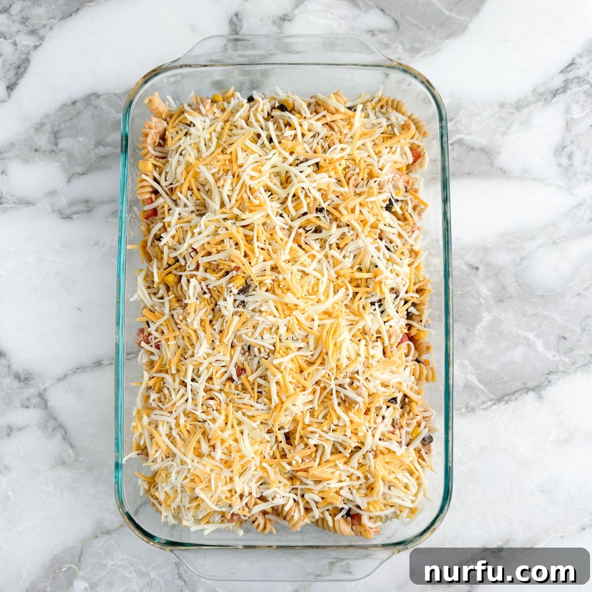 Celebration Chicken Bake 7 Casserole dish with chicken and pasta mixture, topped with shredded cheese, ready for baking.