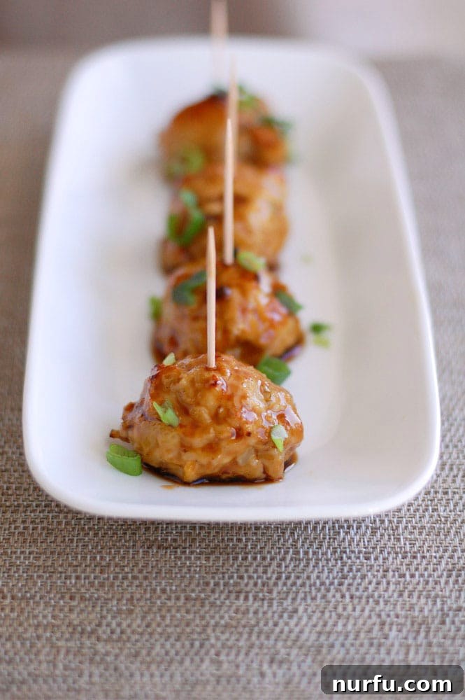 Sticky Pineapple Teriyaki Chicken Meatballs 6 A close-up of a single chicken teriyaki meatball, glistening with sauce and topped with green onions, ready to be enjoyed.
