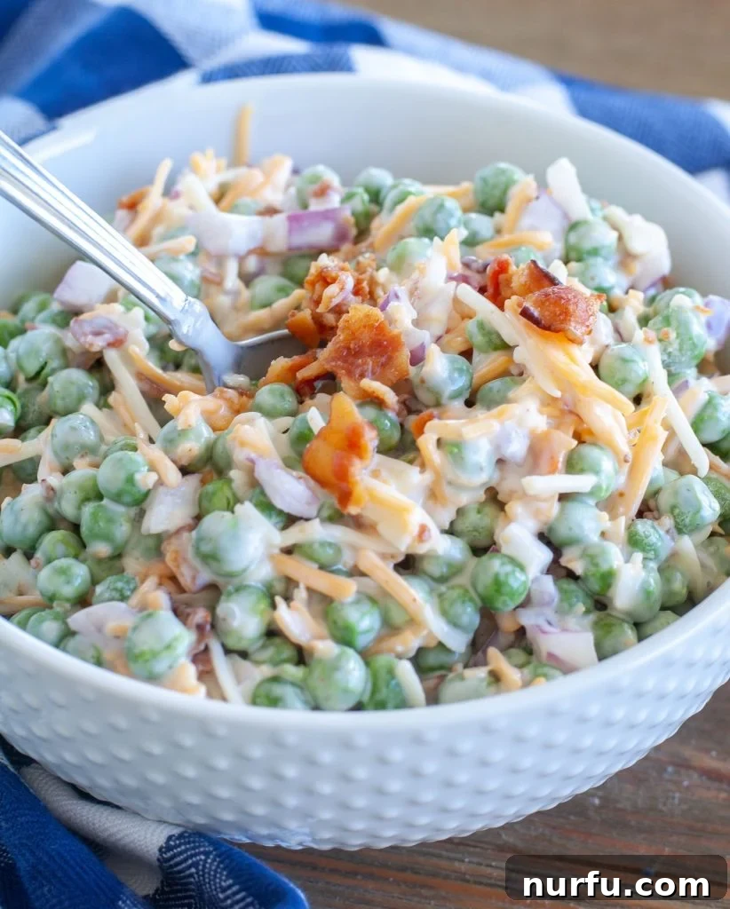 Pea Salad with Bacon Creamy pea salad topped with crispy bacon in a pristine white bowl, ready to be served with a spoon. Perfect for potlucks and family meals.