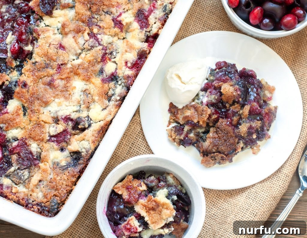 Cranberry Cherry Dump Cake A beautifully presented Cranberry Cherry Dump Cake, with some servings removed, showcasing its delicious texture. A bowl of fresh cranberries and cherries sits nearby, completing the festive scene.