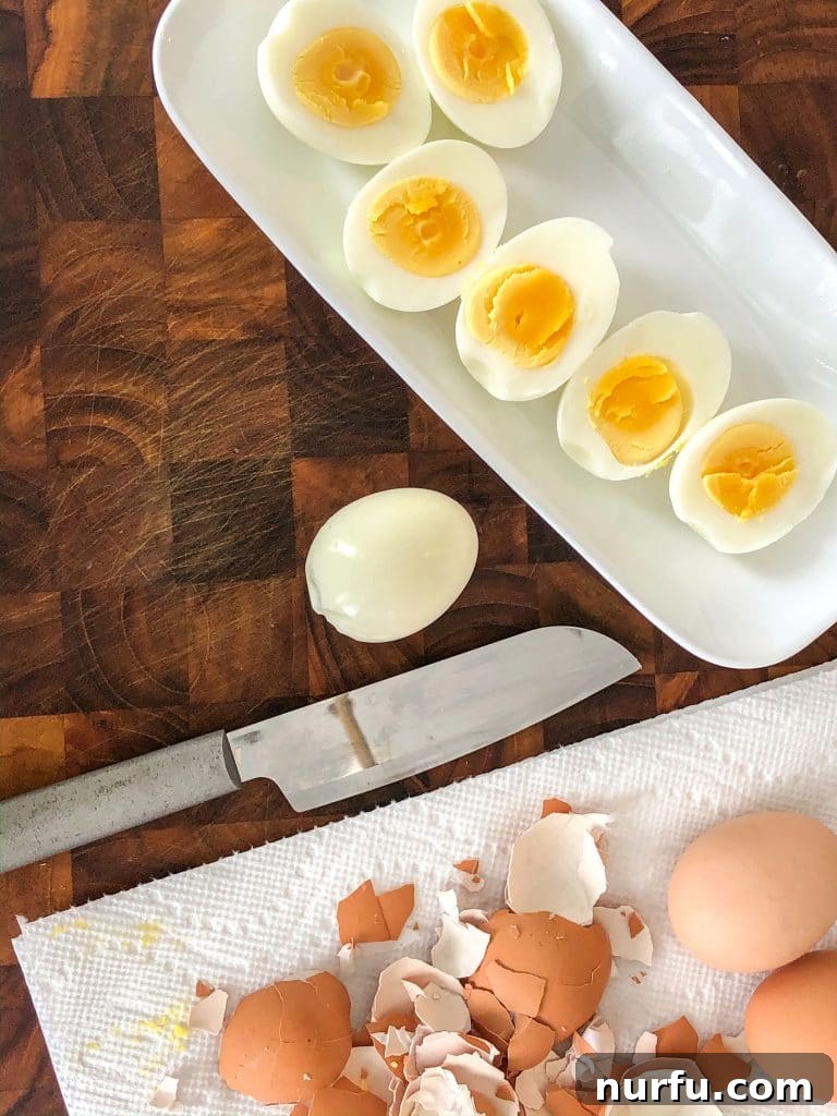 Air Fryer Eggs Made Easy 4 White plate with halved hard-boiled eggs, a knife, and discarded eggshells on a paper towel