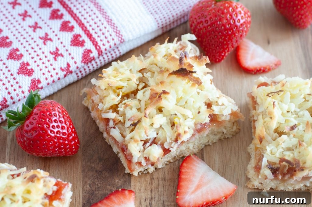 Tropical Strawberry Coconut Bars 2 A perfectly cut strawberry coconut bar garnished with fresh strawberries and a decorative tea towel
