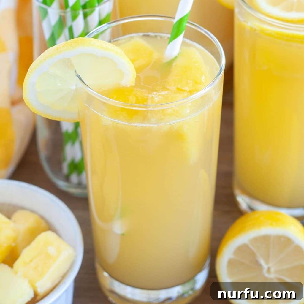 A tall glass of vibrant Pineapple Lemonade garnished with fresh mint and a lemon slice, with a green striped straw.