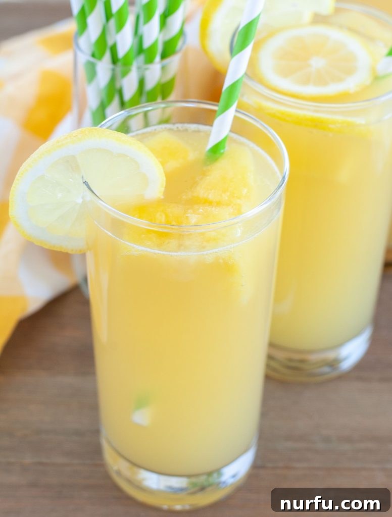Two glasses of Pineapple Lemonade with green striped straws and fresh garnishes.