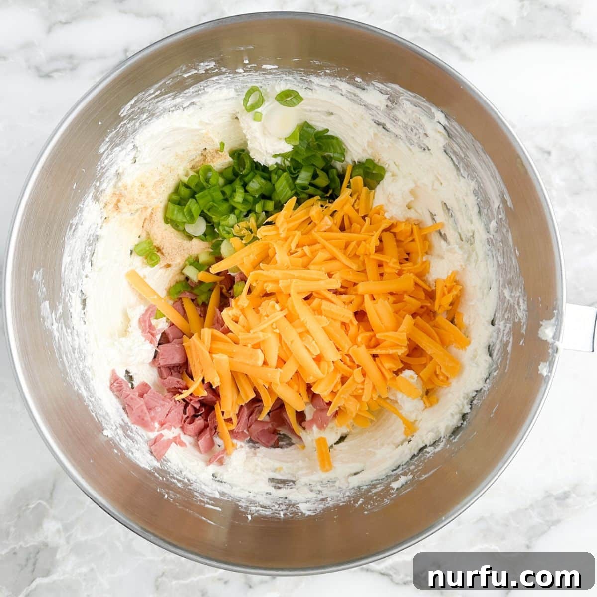 Signature Chipped Beef Cheese Ball 4 A large mixing bowl containing softened cream cheese, shredded cheddar cheese, diced green onions, and finely chopped chipped beef, ready to be combined.