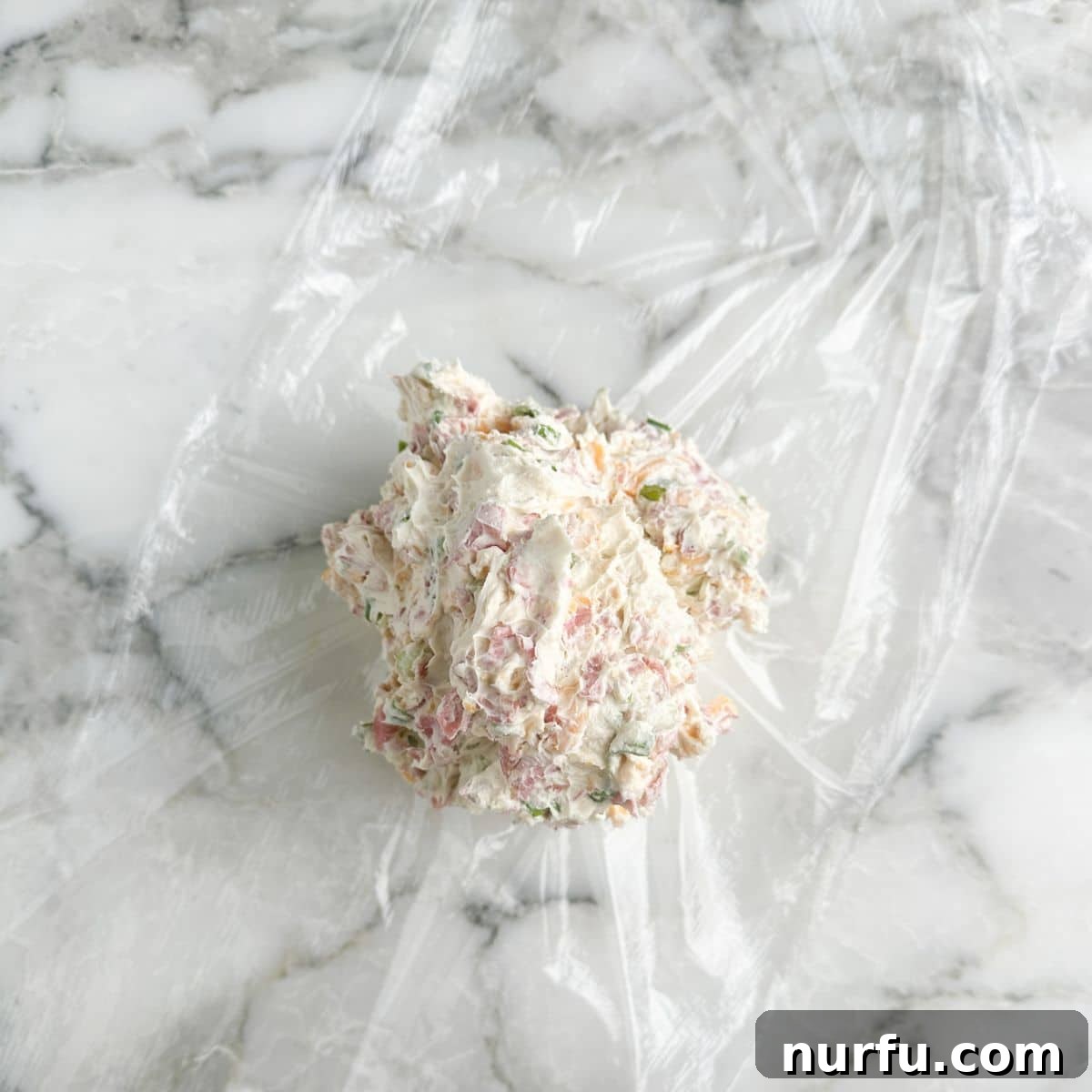 Signature Chipped Beef Cheese Ball 6 The creamy chipped beef cheese ball mixture placed in the center of a large piece of plastic wrap, ready for shaping.