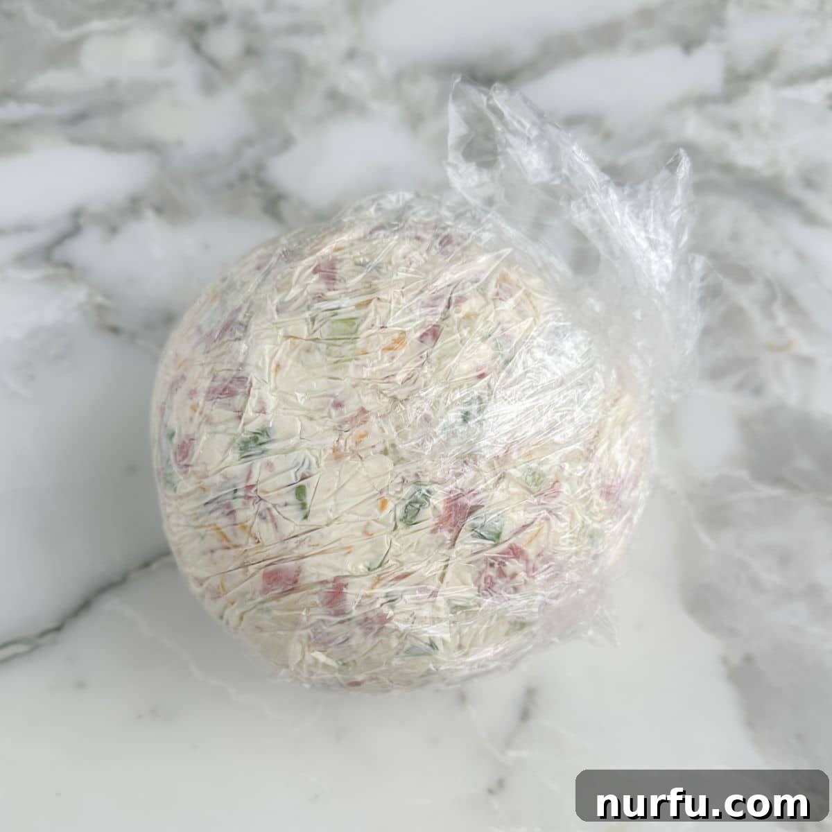 Signature Chipped Beef Cheese Ball 7 A perfectly shaped cheese ball tightly wrapped in plastic wrap, ready for chilling.