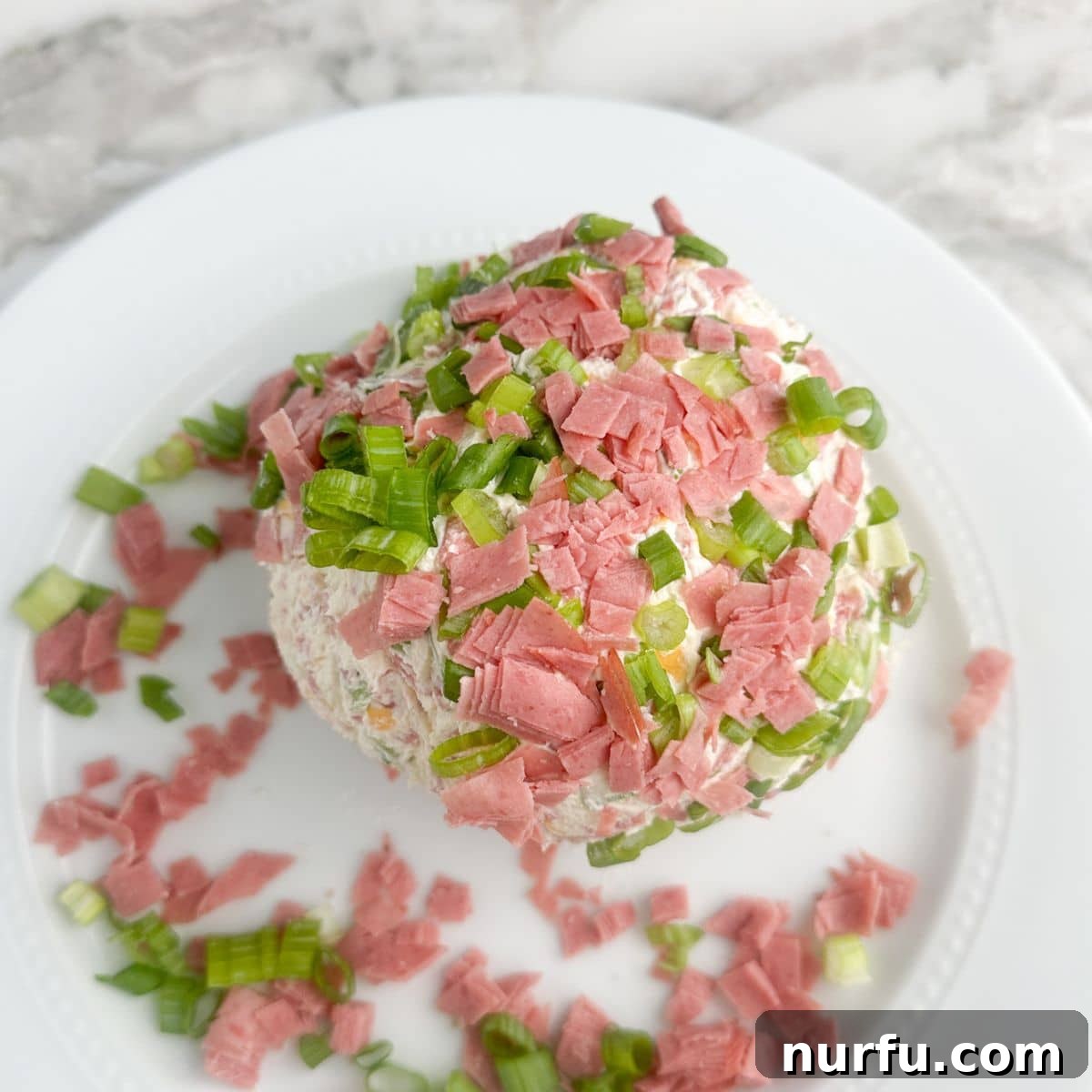 Signature Chipped Beef Cheese Ball 9 Another angle of the garnished Chipped Beef Cheese Ball on a plate, highlighting its appetizing texture and vibrant green onion coating.