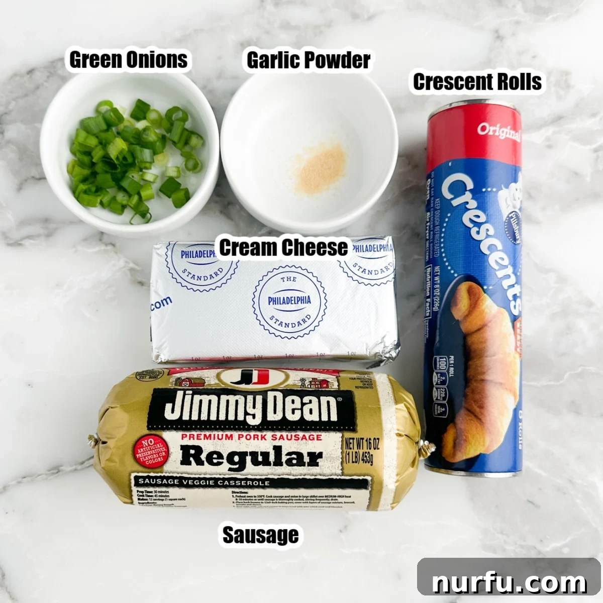 Savory Sausage Spirals 3 Close-up of key ingredients: a roll of breakfast sausage, a can of crescent rolls, a block of softened cream cheese, fresh green onions, and a small bowl of garlic powder, neatly arranged on a counter.