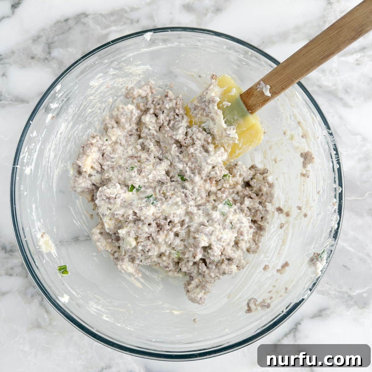 Savory Sausage Spirals 4 A bowl showcasing the creamy and savory mixture of beaten cream cheese, crumbled sausage, diced green onions, and garlic powder, ready to be spread onto crescent dough.