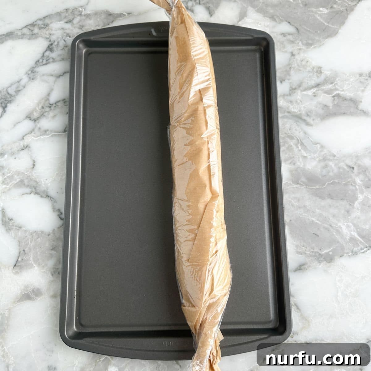 Savory Sausage Spirals 6 A tightly rolled sausage and crescent dough log, wrapped securely in plastic wrap, resting on a baking sheet, prepared for chilling in the freezer.