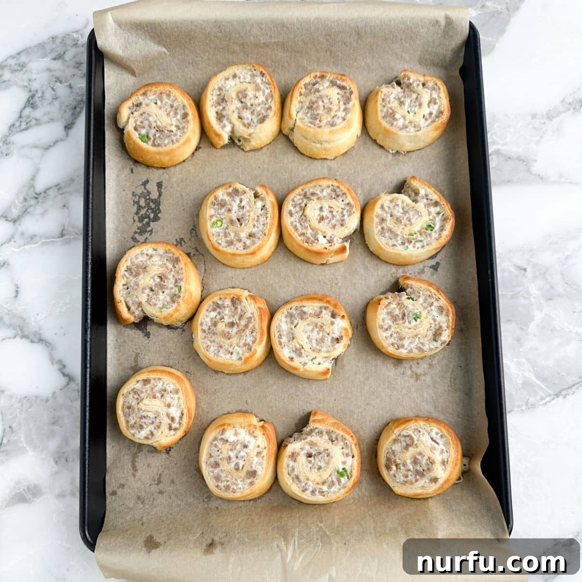 Savory Sausage Spirals 8 A baking sheet filled with golden brown, freshly baked sausage pinwheels, slightly cooled and ready to be enjoyed.