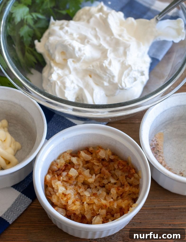 Caramelized Onion Dip 3 Essential ingredients for homemade French Onion Dip: a bowl of sour cream, mayonnaise, freshly diced onions, and various spices arranged on a counter.
