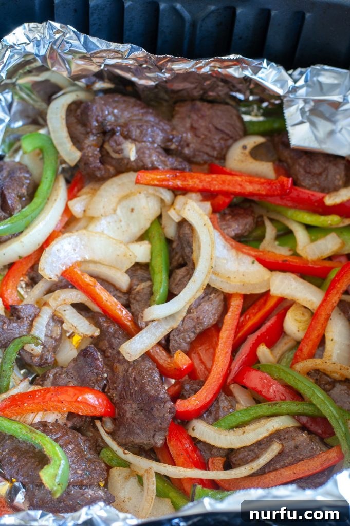 Air Fryer Steak Fajitas - Quick & Easy Recipe Sizzling steak, colorful bell peppers, and onions cooked to perfection in foil inside an air fryer basket, ready for assembly into delicious fajitas.