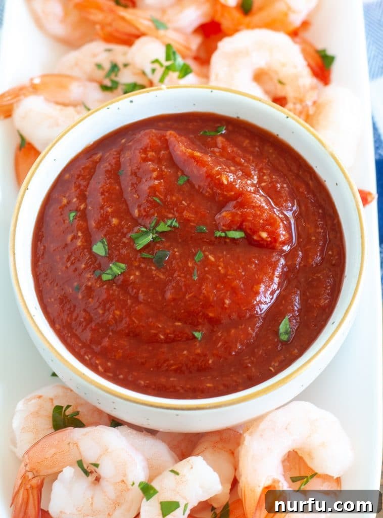 A bowl of vibrant red homemade cocktail sauce, garnished with a sprig of fresh herbs, ready for serving with seafood.